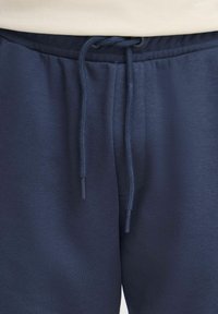 Pantalons de survêtement bleu marine en matériau doux et extensible avec une taille élastique, un cordon de serrage et une texture lisse.