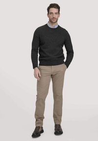 Dunkelgrauer Strickpullover mit Rundhalsausschnitt, beigefarbene Hose und schwarze Schnürstiefel. Das Model steht mit neutraler Körperhaltung vor einem hellen Hintergrund.