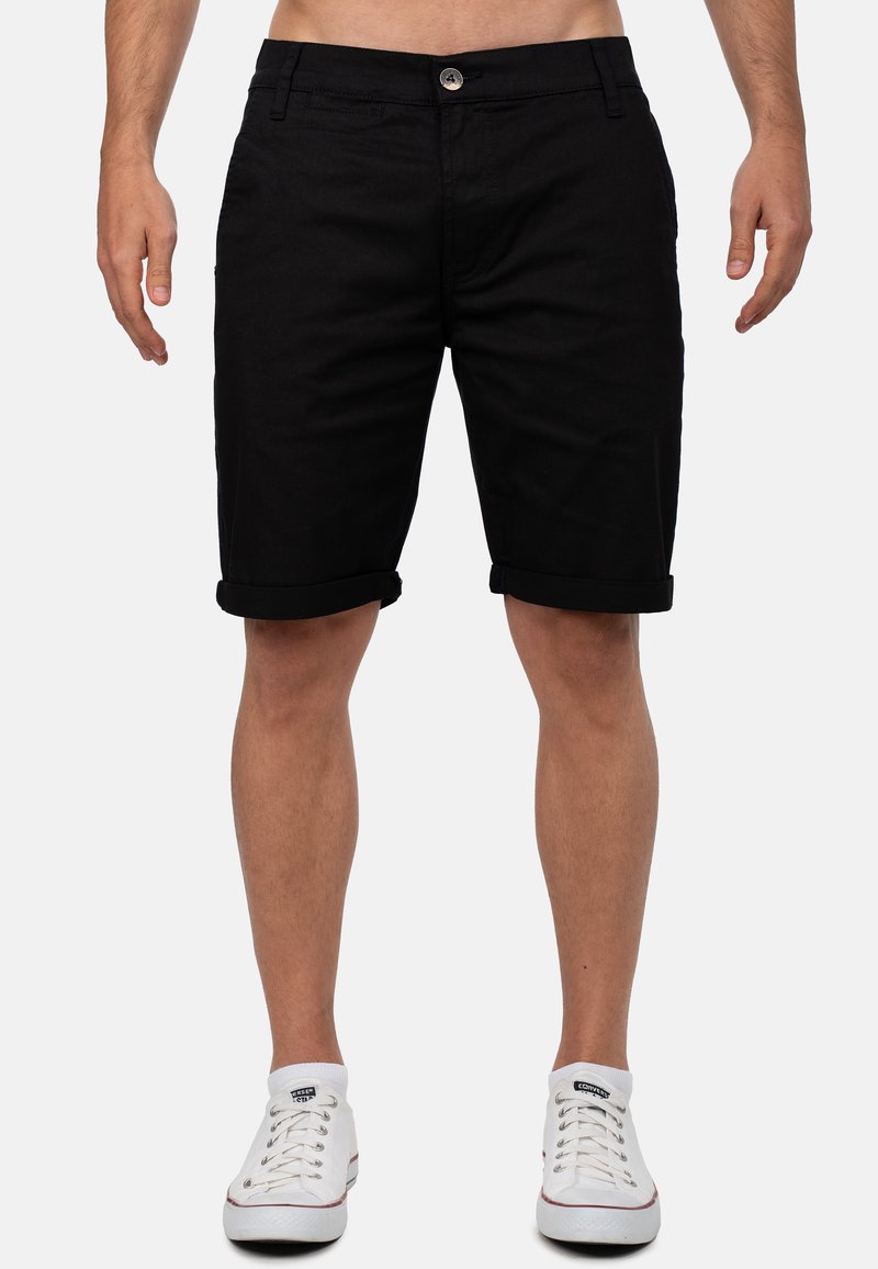 Shorts en coton noir avec des revers roulés, fermeture à bouton et poches avant, présentant une texture lisse et une coupe ajustée.