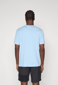 Camisa de manga corta azul claro hecha de material suave, con cuello redondeado y corte relajado, combinada con pantalones cortos negros.
