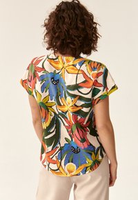 Bluză cu mâneci scurte, cu un model floral în culori vibrante. Confecționată dintr-un material ușor, având flori mari și frunze verzi.
