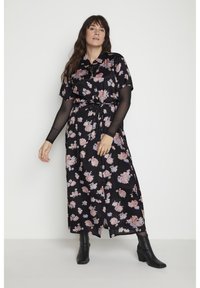 Czarna midi sukienka w kwiaty z krótkimi rękawami, przewiązywana w talii, z guzikiem z przodu; posiada różowe i niebieskie wzory kwiatowe na miękkim materiale. Noszona z czarnymi botkami.
