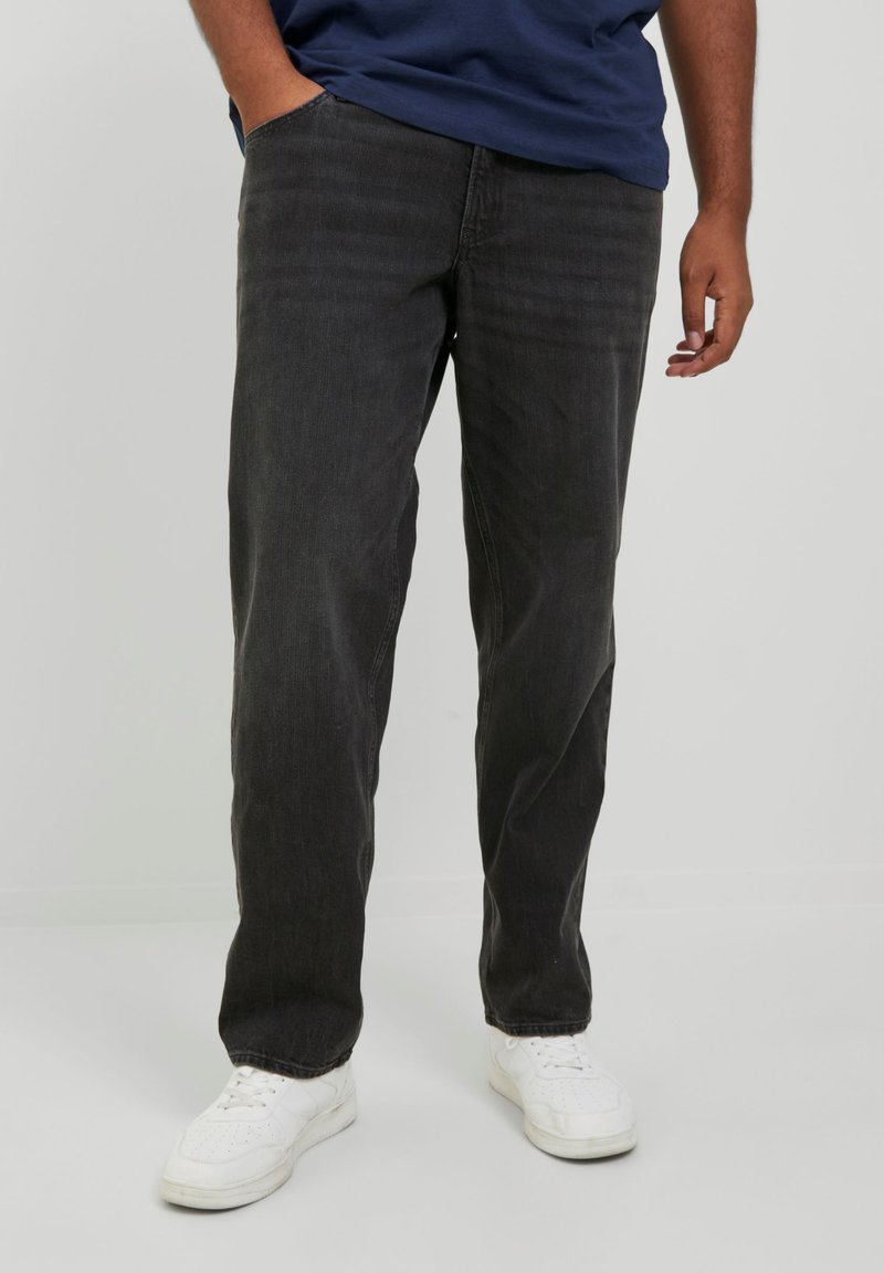 Jean en denim noir avec une coupe décontractée, pr�ésentant un design à cinq poches et un motif texturé subtil, associés à des baskets blanches.