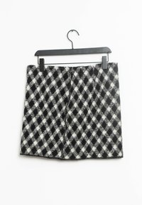 Falda a cuadros en blanco y negro hecha de una tela suave. Presenta un corte recto, colgando de una percha de plástico negro.