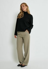 Černý rolák s dlouhými rukávy, v kombinaci s širokými béžovými kalhotami a černými plochými botami, s hladkou texturou a uvolněným střihem.