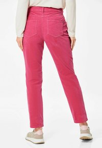 Roze corduroybroek met een recht model, twee achterzakken en een hoge taille. Draagt met grijze sneakers met roze accenten.