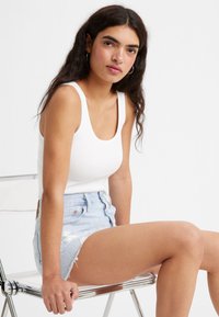 Hvid ribbet tanktop med rund halsudskæring, paired med højtaljede lyseblå denimshorts med en frynsede kant og slidte detaljer.