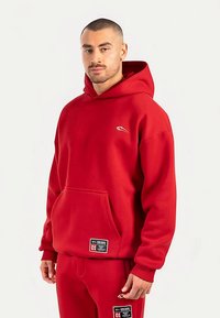 Felpa con cappuccio rossa in tessuto spesso, dotata di una tasca frontale e di un logo. Progettata con una vestibilità comoda e un cappuccio con coulisse regolabile.