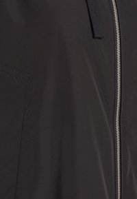 Zwarte bomberjack met een gladde textuur, zilveren rits en capuchonontwerp. Bevat subtiele stikdetails en een strakke silhouet.