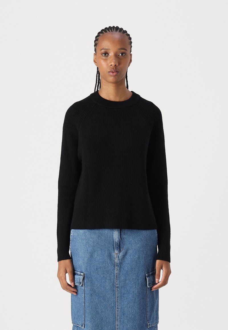 Schwarzer gerippter Pullover mit rundem Ausschnitt, langen Ärmeln und lockerer Passform, kombiniert mit einem Jeansrock mit frontalen Taschen.