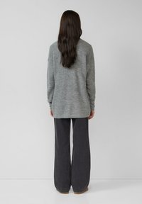 Grauer, strukturierter Strickpullover mit lockerer Passform, kombiniert mit weiten, dunklen Hosen, die die Rückansicht und den glatten Stoff zeigen.