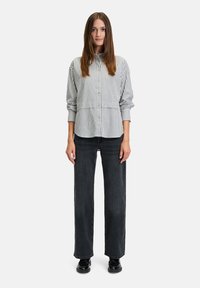 Gestreiftes Hemd in Weiß und Marineblau mit abgerundetem Saum, kombiniert mit hochgeschnittenen, weiten, dunkelblauen Jeans. Schwarze Schuhe runden den Look ab.