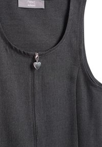 Robe noire sans manches avec un col rond et un tissu texturé subtil. Présente une fermeture éclair centrale avec un tirette en forme de cœur.