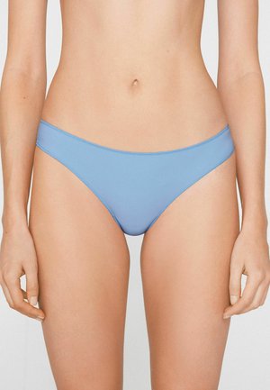 Frau trägt einfache hellblaue Bikini-Unterwäsche, gezeigt vom Taillenbereich bis zu den oberen Oberschenkeln, steht mit entspannten Armen an den Seiten.