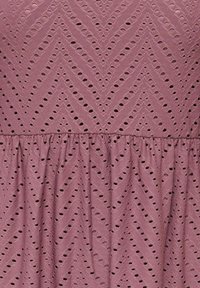 Mauve fabric with eyelet embroidery forming chevron and triangular patterns, featuring gathered seam detail across the middle.