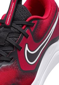 Chaussure de sport rouge et noire avec un dessus en mailles et synthétique, système de laçage et logo Swoosh Nike blanc. Semelle blanche rembourrée.