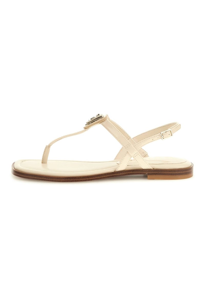 Beige sandal med ett tunt rem och justerbar ankelspänne. Har en platt sula och en dekorativ accent fram. Slät yta.