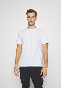 T-shirt blanc en coton à manches courtes. Présente un petit logo gris sur la poitrine gauche. Encolure ronde simple, coupe décontractée.