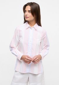 White button-up shirt featuring vertical red and blue stripes, long sleeves, and a classic collar, paired with light-colored pants.