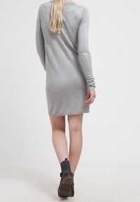 Abito a maglia grigio a maniche lunghe con vestibilità rilassata, dotato di polsini a coste e orlo arrotondato, abbinato a stivaletti neri a caviglia.
