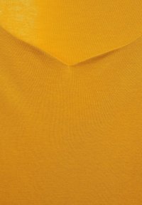Žlutá látka s texturovaným povrchem, s výstřihem ve tvaru V a hladkým, jednotným odstínem.
