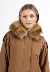 Bruine jas met een grote faux fur kraag in oranje en zwarte tinten. Het ontwerp heeft een sluiting aan de voorkant en schouderaccenten.
