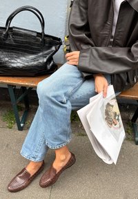 Pruunist tekstuuriga nahast korterid, millel on kootud muster, koos helesiniste sirgete pükste jaama. Lähistel lebab must krokodillimuster kott.