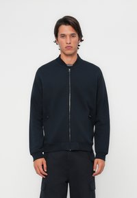 Veste bomber zippée bleu marine avec col rond, dotée de poches latérales et de poignets côtelés, fabriquée en tissu lisse et doux.