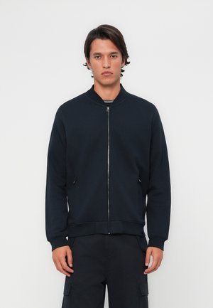 Veste bomber zippée bleu marine avec col rond, dotée de poches latérales et de poignets côtelés, fabriquée en tissu lisse et doux.