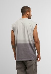 Ärmelloses T-Shirt mit Gradient in Hellgrau, das in Dunkelgrau übergeht, kombiniert mit grauen Cargo-Shorts. Weiches, leichtes Material, lässiges Design.