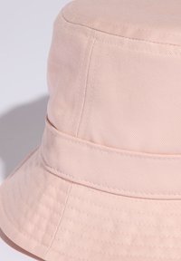 Světle růžový bavlněný klobouk s viditelným šitím a širokým, dolů skloněným okrajem na jednobarevném světlém pozadí.