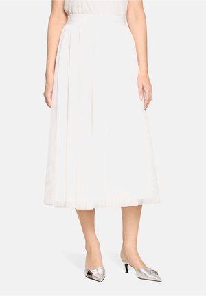 Jupe midi plissée blanche avec une texture lisse et une large ceinture, associée à des escarpins argentés à bout pointu.