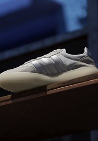 Vue latérale en contre-plongée d'une basket blanche et beige avec trois bandes sur une surface en bois sur fond sombre flou.