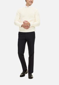 Maglione a treccia crema, camicia bianca con colletto, pantaloni scuri e mocassini neri. Vestibilità casual con motivi testurizzati sul maglione.