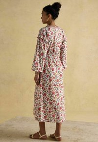 Kleid mit Blumenmuster, langen Ärmeln, geraffter Taille und Knopfdetail am Rücken. Hergestellt aus leichtem Stoff in Weiß mit roten und grünen Motiven.