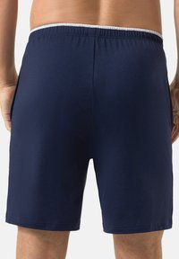 Shorts de bain bleu marine avec une taille élastique, présentant un accent blanc en haut, fabriqués en tissu doux et lisse, avec des poches latérales.