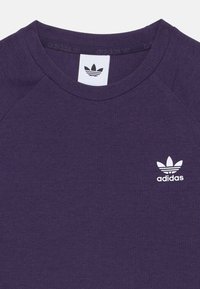 Lila bordázott pamut t-shirt kerek nyakkal és fehér Adidas logóval, amely három levelet ábrázol a bal mellrészen.