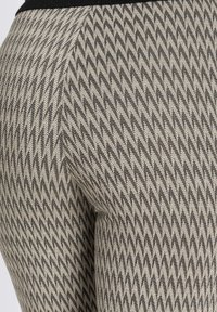 Tkany materiał w deseń houndstooth w odcieniach beżu i czerni, dopasowany krój z wyraźną teksturą i kontrastowym detalem w pasie.