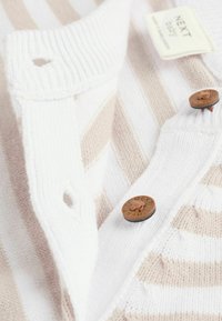 Lekki sweter w białe i beżowe paski z rypsowym kołnierzykiem, dwoma brązowymi guzikami oraz małą metką wskazującą markę.