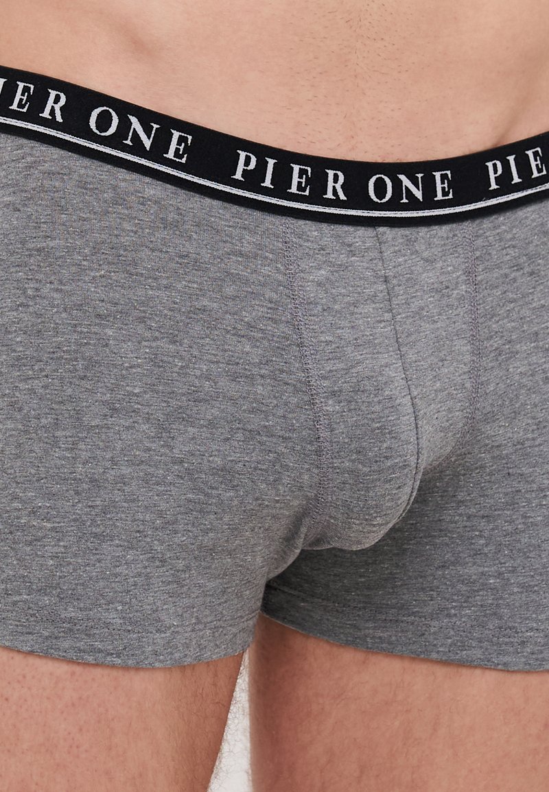 Boxers grises hechos de una tela suave, con una cinturilla negra que lleva "PIER ONE" en texto blanco. Textura lisa con un diseño ajustado.