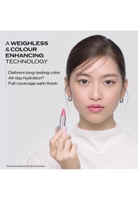 Woman with subtle makeup holds pink lipstick, promoting weightless, color-enhancing technology with long-lasting color and hydration.