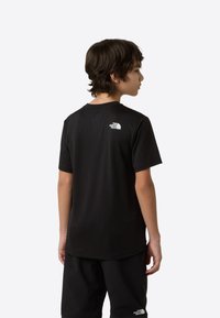 Μαύρο μπλουζάκι με κοντά μανίκια, με στρογγυλή λαιμόκοψη και μικρό λευκό λογότυπο στο πίσω μέρος. Το ύφασμα φαίνεται λείο και ελαφρύ.