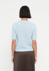 Φωτεινό γαλάζιο πλεκτό πουλόβερ με κοντά μανίκια, με σχέδιο διάτρητου ρόμβου και ριμπ τελείωμα. Η πίσω όψη δείχνει λεπτομερή υφή.