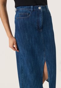 Denim krilo v temno modri barvi s prednjim razporkom, z gumbom, diskretno podrobnostjo žepov in gladko teksturo.