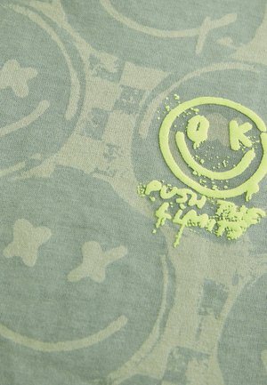 Tissu en coton vert avec un motif texturé, comportant un visage souriant jaune et la phrase "poussez vos limites" en jaune.