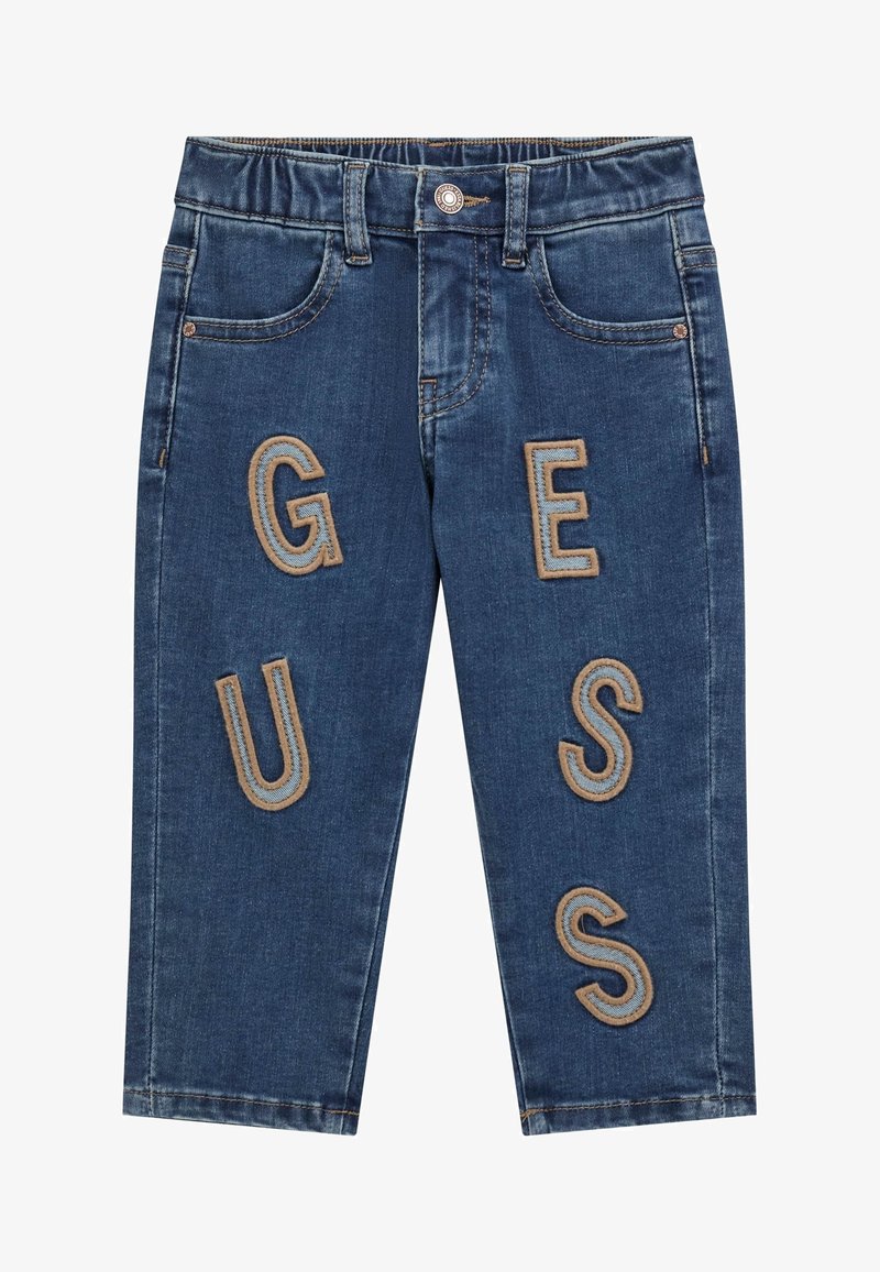 Denim-Jeans mit einer dunkelblauen Waschung, ausgestattet mit großen, gestickten Buchstaben "G", "U", "E", "S", "S" in einer kontrastierenden sandfarbenen Farbe. Klassisches Fünf-Taschen-Design.