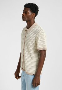 Kortärmad stickad polo i beige med ett strukturerat mönster, kontrasterande krage och fem knappar framtill.
