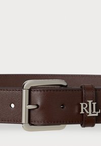 Ruskea nahkavyö, jossa on hopeinen metallinen solki, kiiltävällä pinnalla ja kaiverrettu "RL"-logo vyön nauhassa.