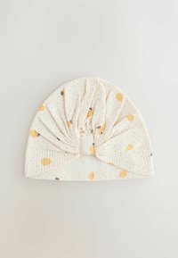 Gorro blanco suave para bebé con textura acanalada y pequeño estampado de fruta amarilla, con un diseño de nudo recogido en el centro frontal.