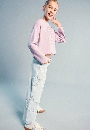 Světle fialová krátká mikina s květinovým vzorem, doplněná světle modrými džínami s dvěma hvězdnými nášivkami. Outfit je dokončen bílými teniskami.